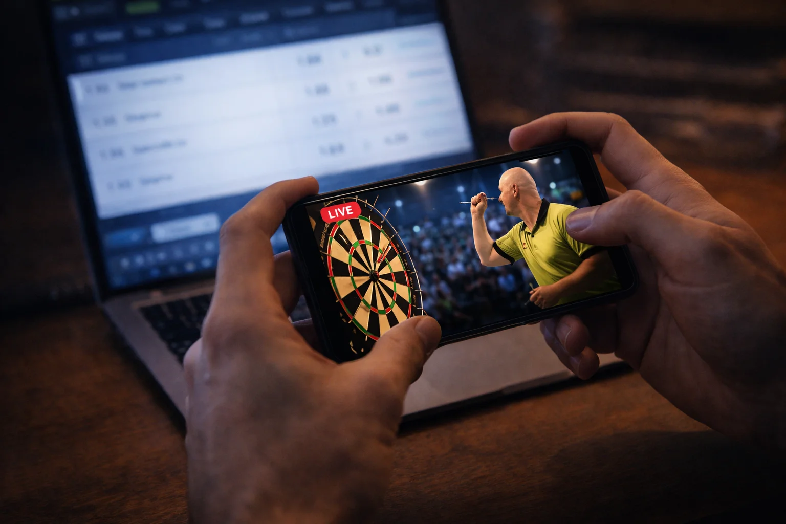 Smartphone zeigt einen Darts-Livestream neben einem Laptop mit Wettquoten